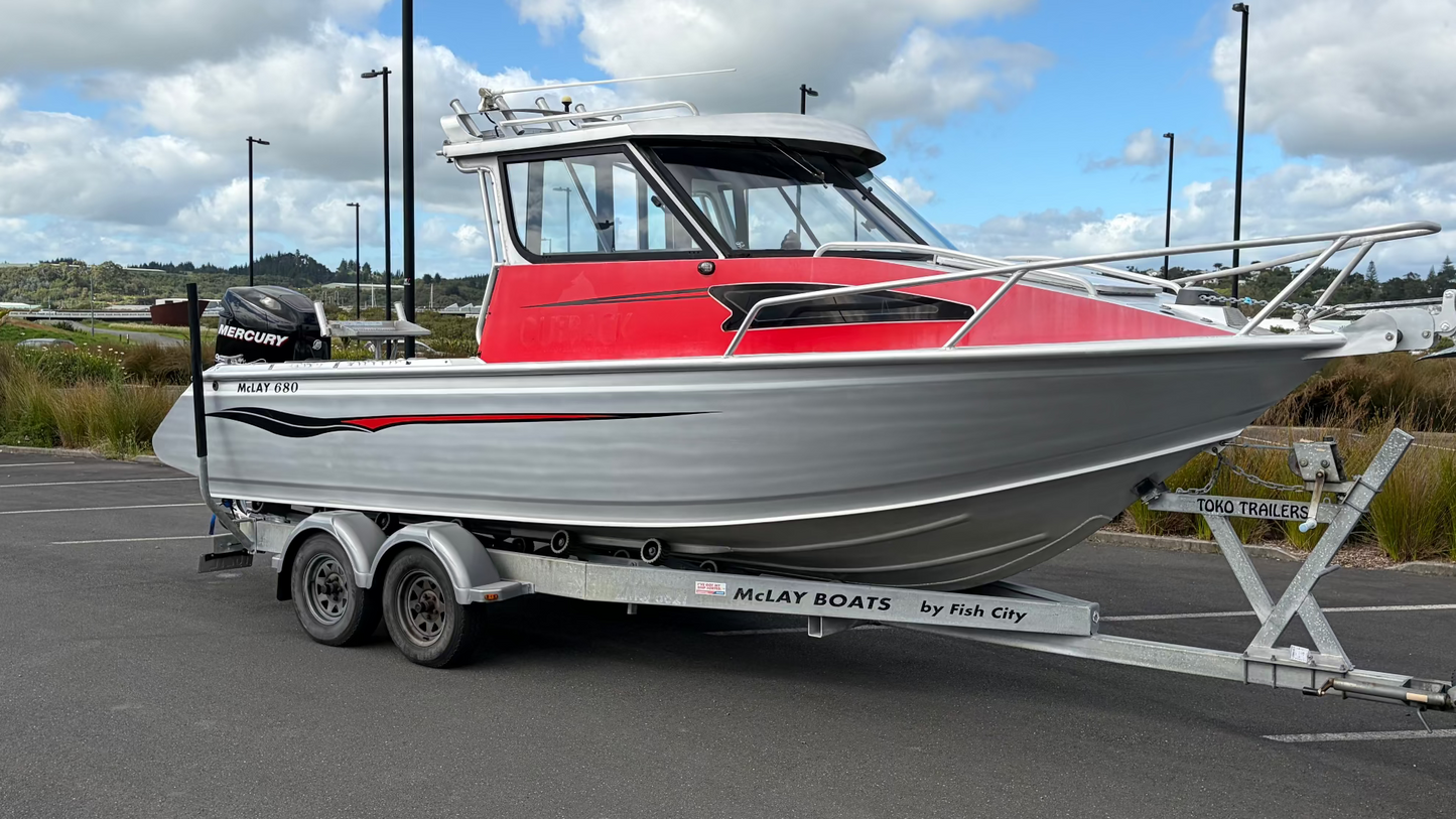 Used 2010 McLay 680 hardtop boat powered by a 225hp Mercury Optimax outboard, sitting on a tandem-axle Toko trailer. Features include boarding ladder, bait board, trim tabs, step mounts, livebait tank, twin batteries with VSR and isolation switch, GME VHF, Lowrance HDS 8, and 170L underfloor fuel tank. Warren Hay Marine, Whangarei