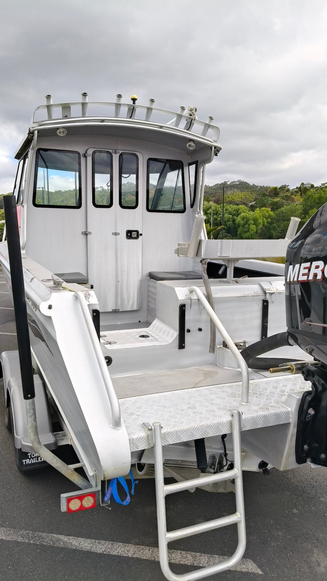 Used 2010 McLay 680 hardtop boat powered by a 225hp Mercury Optimax outboard, sitting on a tandem-axle Toko trailer. Features include boarding ladder, bait board, trim tabs, step mounts, livebait tank, twin batteries with VSR and isolation switch, GME VHF, Lowrance HDS 8, and 170L underfloor fuel tank. Warren Hay Marine, Whangarei