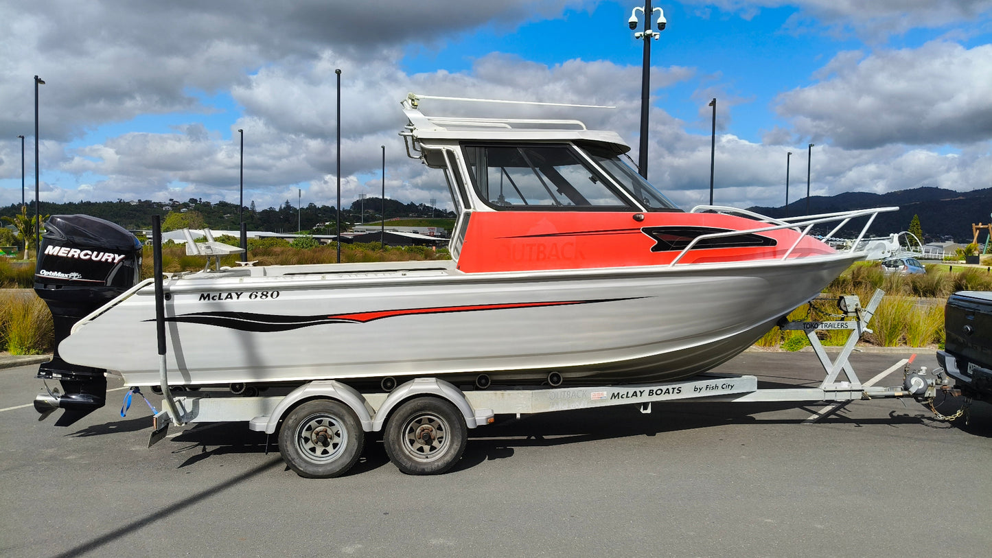 Used 2010 McLay 680 hardtop boat powered by a 225hp Mercury Optimax outboard, sitting on a tandem-axle Toko trailer. Features include boarding ladder, bait board, trim tabs, step mounts, livebait tank, twin batteries with VSR and isolation switch, GME VHF, Lowrance HDS 8, and 170L underfloor fuel tank. Warren Hay Marine, Whangarei