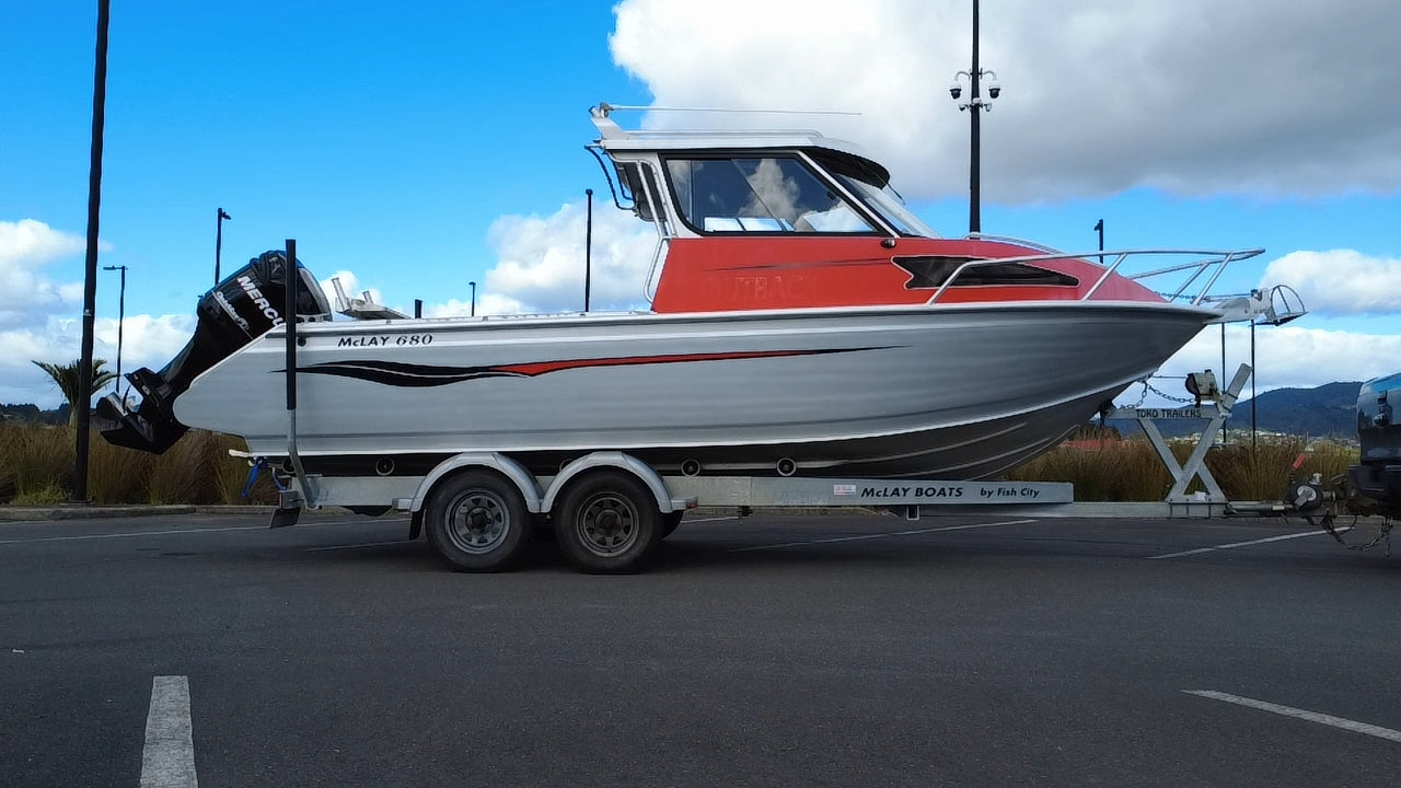Used 2010 McLay 680 hardtop boat powered by a 225hp Mercury Optimax outboard, sitting on a tandem-axle Toko trailer. Features include boarding ladder, bait board, trim tabs, step mounts, livebait tank, twin batteries with VSR and isolation switch, GME VHF, Lowrance HDS 8, and 170L underfloor fuel tank. Warren Hay Marine, Whangarei