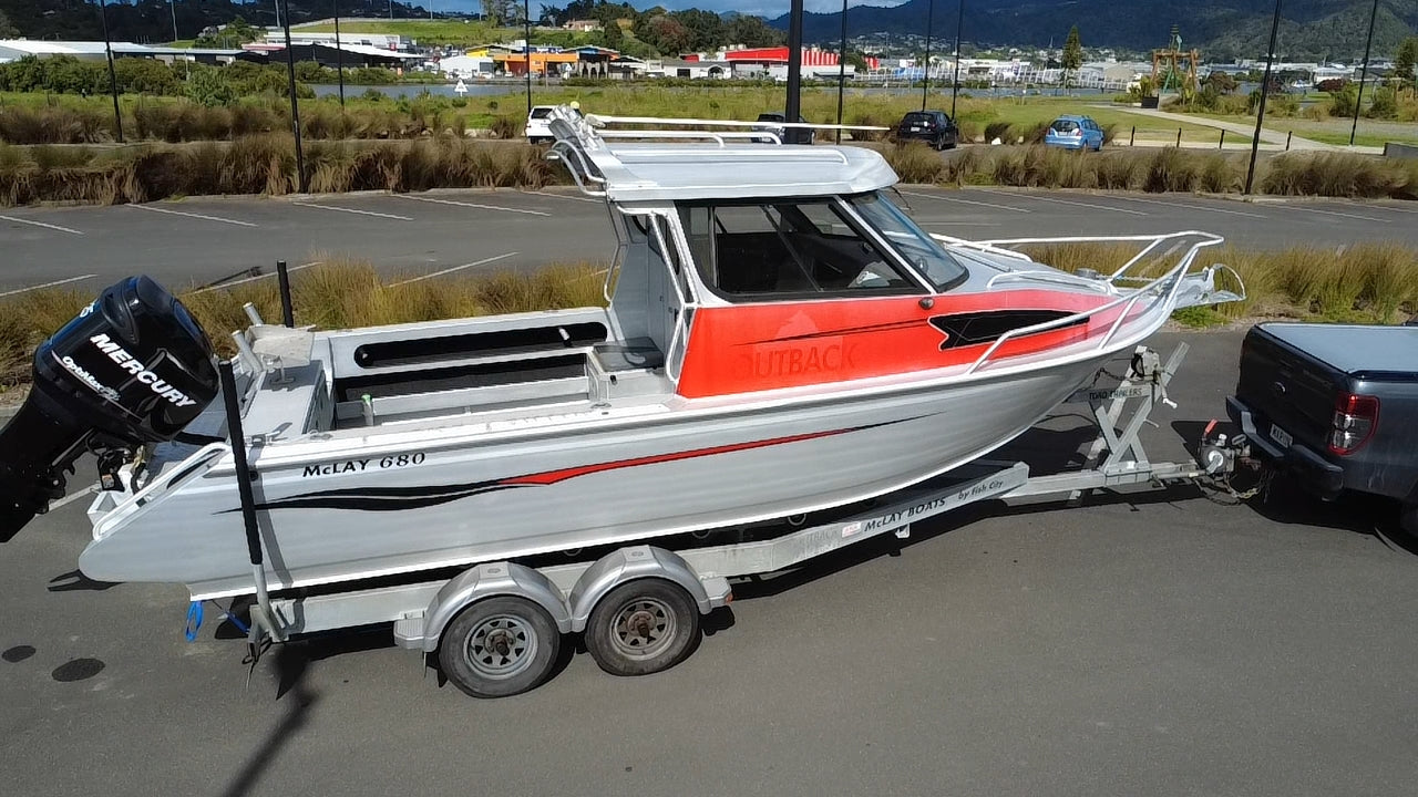 Used 2010 McLay 680 hardtop boat powered by a 225hp Mercury Optimax outboard, sitting on a tandem-axle Toko trailer. Features include boarding ladder, bait board, trim tabs, step mounts, livebait tank, twin batteries with VSR and isolation switch, GME VHF, Lowrance HDS 8, and 170L underfloor fuel tank. Warren Hay Marine, Whangarei