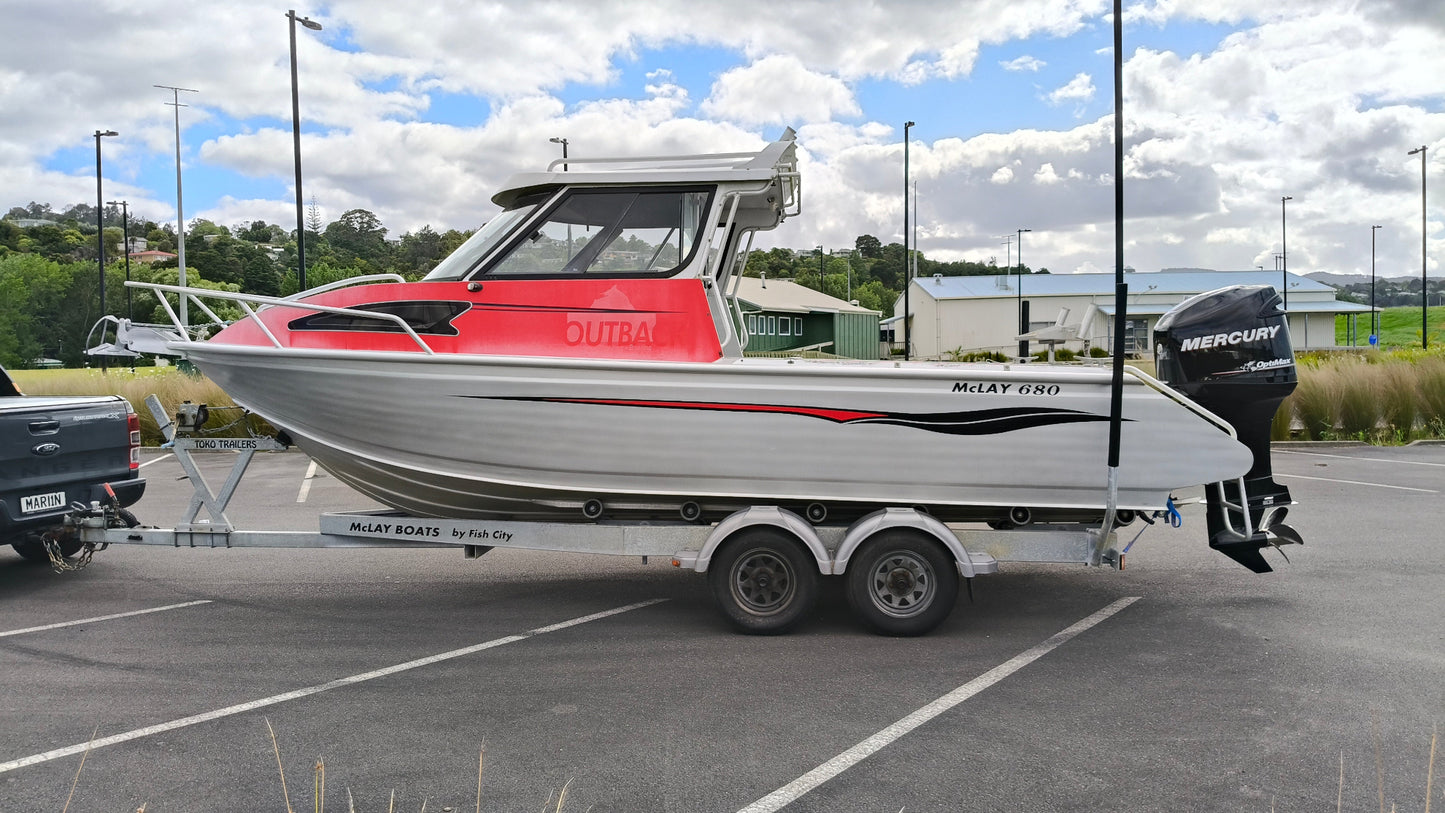Used 2010 McLay 680 hardtop boat powered by a 225hp Mercury Optimax outboard, sitting on a tandem-axle Toko trailer. Features include boarding ladder, bait board, trim tabs, step mounts, livebait tank, twin batteries with VSR and isolation switch, GME VHF, Lowrance HDS 8, and 170L underfloor fuel tank. Warren Hay Marine, Whangarei