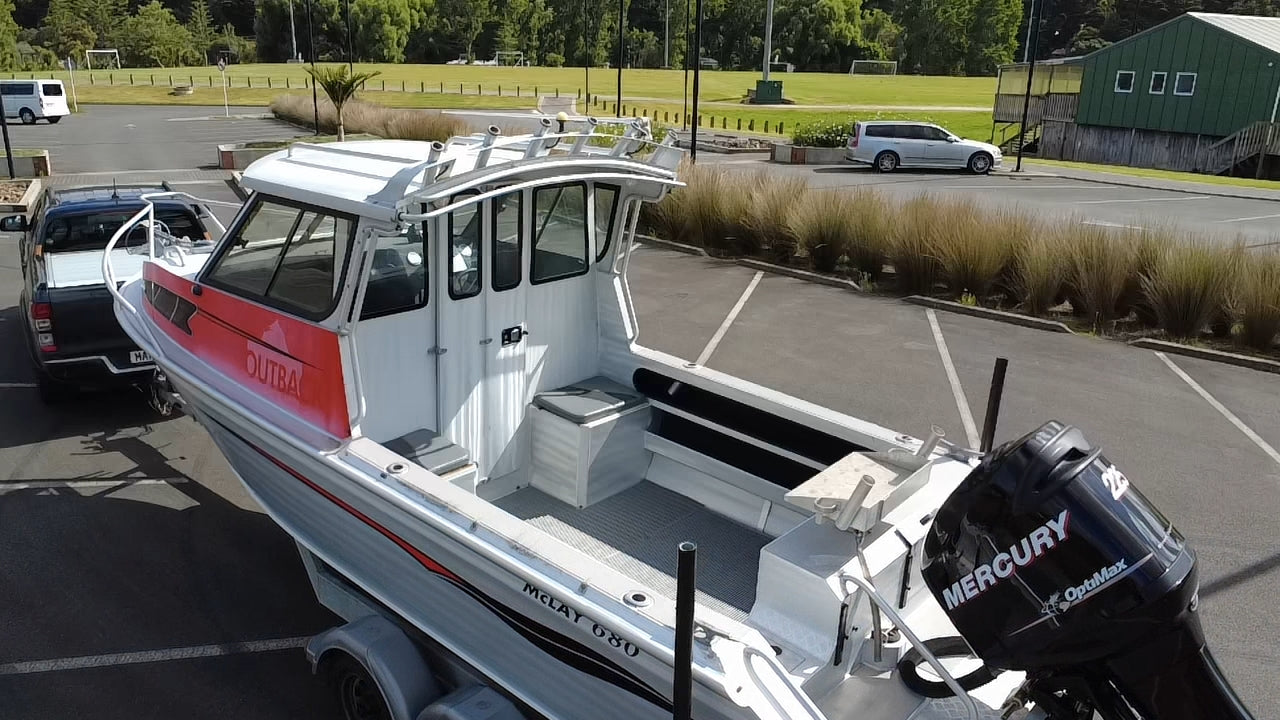 Used 2010 McLay 680 hardtop boat powered by a 225hp Mercury Optimax outboard, sitting on a tandem-axle Toko trailer. Features include boarding ladder, bait board, trim tabs, step mounts, livebait tank, twin batteries with VSR and isolation switch, GME VHF, Lowrance HDS 8, and 170L underfloor fuel tank. Warren Hay Marine, Whangarei