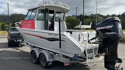 Used 2010 McLay 680 hardtop boat powered by a 225hp Mercury Optimax outboard, sitting on a tandem-axle Toko trailer. Features include boarding ladder, bait board, trim tabs, step mounts, livebait tank, twin batteries with VSR and isolation switch, GME VHF, Lowrance HDS 8, and 170L underfloor fuel tank. Warren Hay Marine, Whangarei