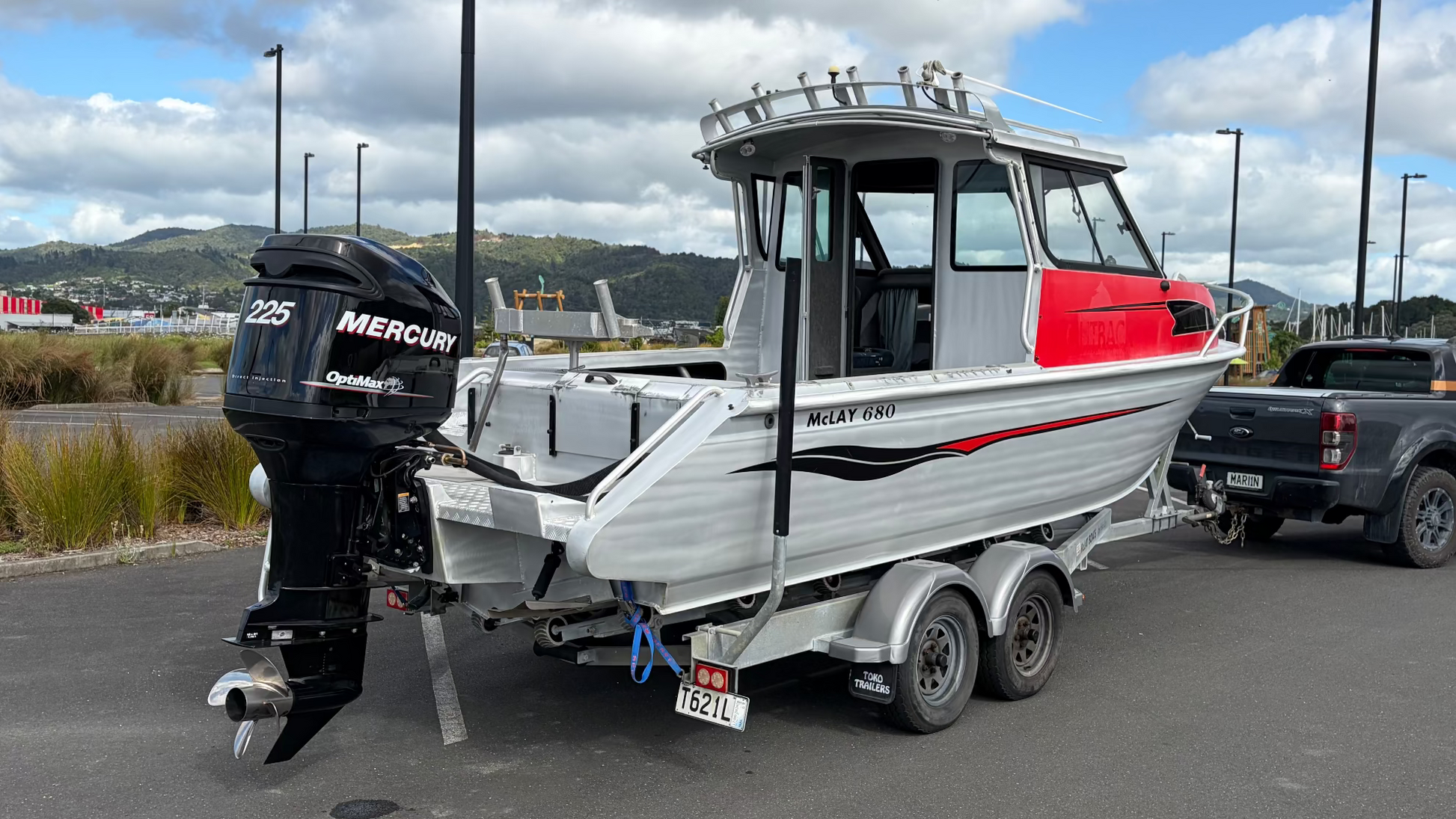 Used 2010 McLay 680 hardtop boat powered by a 225hp Mercury Optimax outboard, sitting on a tandem-axle Toko trailer. Features include boarding ladder, bait board, trim tabs, step mounts, livebait tank, twin batteries with VSR and isolation switch, GME VHF, Lowrance HDS 8, and 170L underfloor fuel tank. Warren Hay Marine, Whangarei