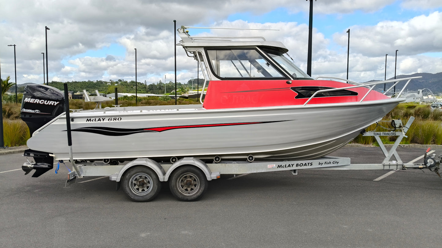 Used 2010 McLay 680 hardtop boat powered by a 225hp Mercury Optimax outboard, sitting on a tandem-axle Toko trailer. Features include boarding ladder, bait board, trim tabs, step mounts, livebait tank, twin batteries with VSR and isolation switch, GME VHF, Lowrance HDS 8, and 170L underfloor fuel tank. Warren Hay Marine, Whangarei