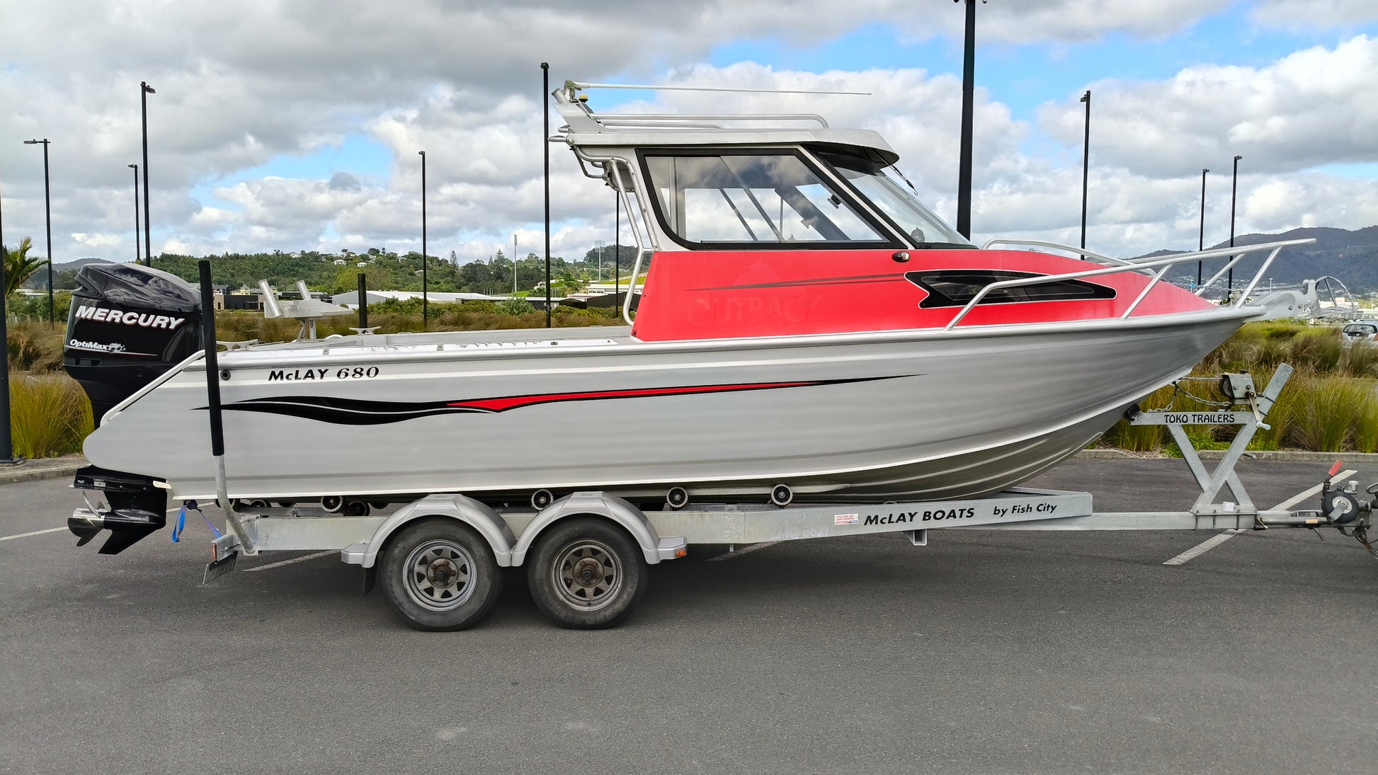 Used 2010 McLay 680 hardtop boat powered by a 225hp Mercury Optimax outboard, sitting on a tandem-axle Toko trailer. Features include boarding ladder, bait board, trim tabs, step mounts, livebait tank, twin batteries with VSR and isolation switch, GME VHF, Lowrance HDS 8, and 170L underfloor fuel tank. Warren Hay Marine, Whangarei