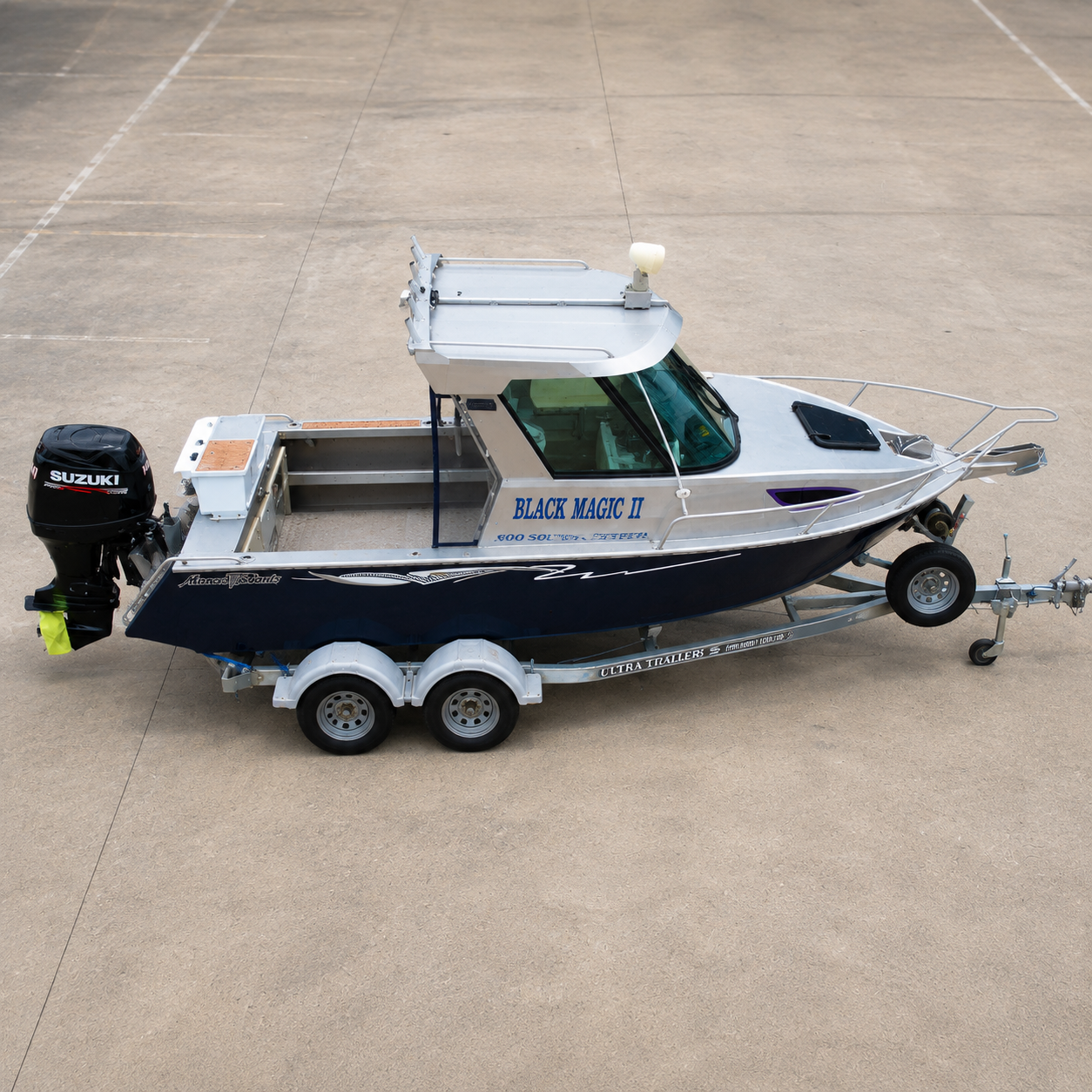 Used Boats, High-angle aerial view of a 2018 Marco 600 Sou'Wester Hard Top with Suzuki BF140 four-stroke outboard on an Ultra Trailers tandem axle trailer, highlighting the cockpit layout, hardtop, and bow platform at Warren Hay Marine, Whangārei.